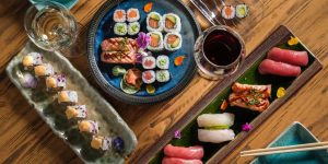 Top view of delicious various sushi and rolls with fish served on wooden table with chopsticks and wineglasses with alcohol drinks